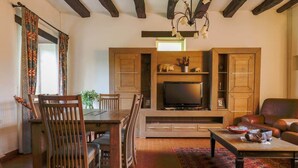 A living room with a wooden TV stand, a dining table with chairs, a sofa, and a patterned rug.