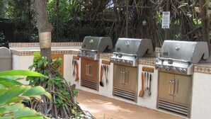 A patio area with three barbecue grills, a stone pathway, and a variety of plants. - Direct Oceanfront Studio With Private Lanai (Lahaina)