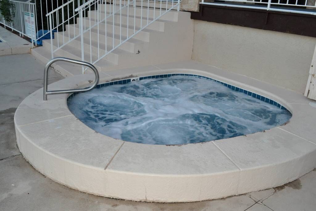 Un jacuzzi con una escalera metálica y un borde de azulejos, rodeado por una terraza de concreto.