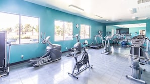A gym with various exercise equipment, large windows, and a view of the outside.