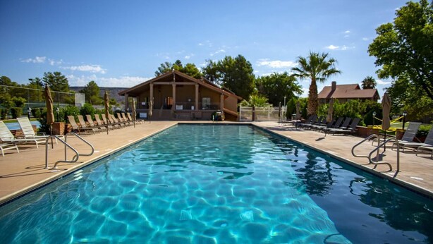 A rectangular swimming pool with clear blue water, surrounded by lounge chairs and a building with a sloped roof.