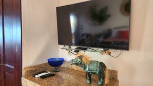 Un televisor montado en la pared, una encimera de granito, un tazón azul y una estatua decorativa de un caballo.