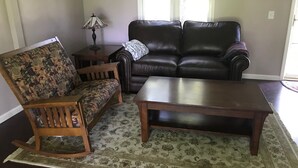 Ein Wohnzimmer mit einem Holzschaukelstuhl, einem schwarzen Ledersofa und einem Holztisch.