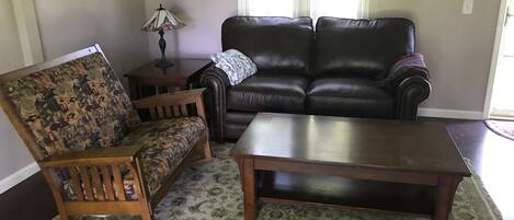 Un salon avec un fauteuil à bascule en bois, un canapé en cuir noir et une table basse en bois.