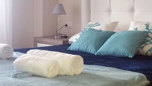A neatly made bed with blue and white bedding, a bedside lamp, and a rolled towel on the floor. - Manilva Playa luxury apartment with sea view near the beach (Manilva)