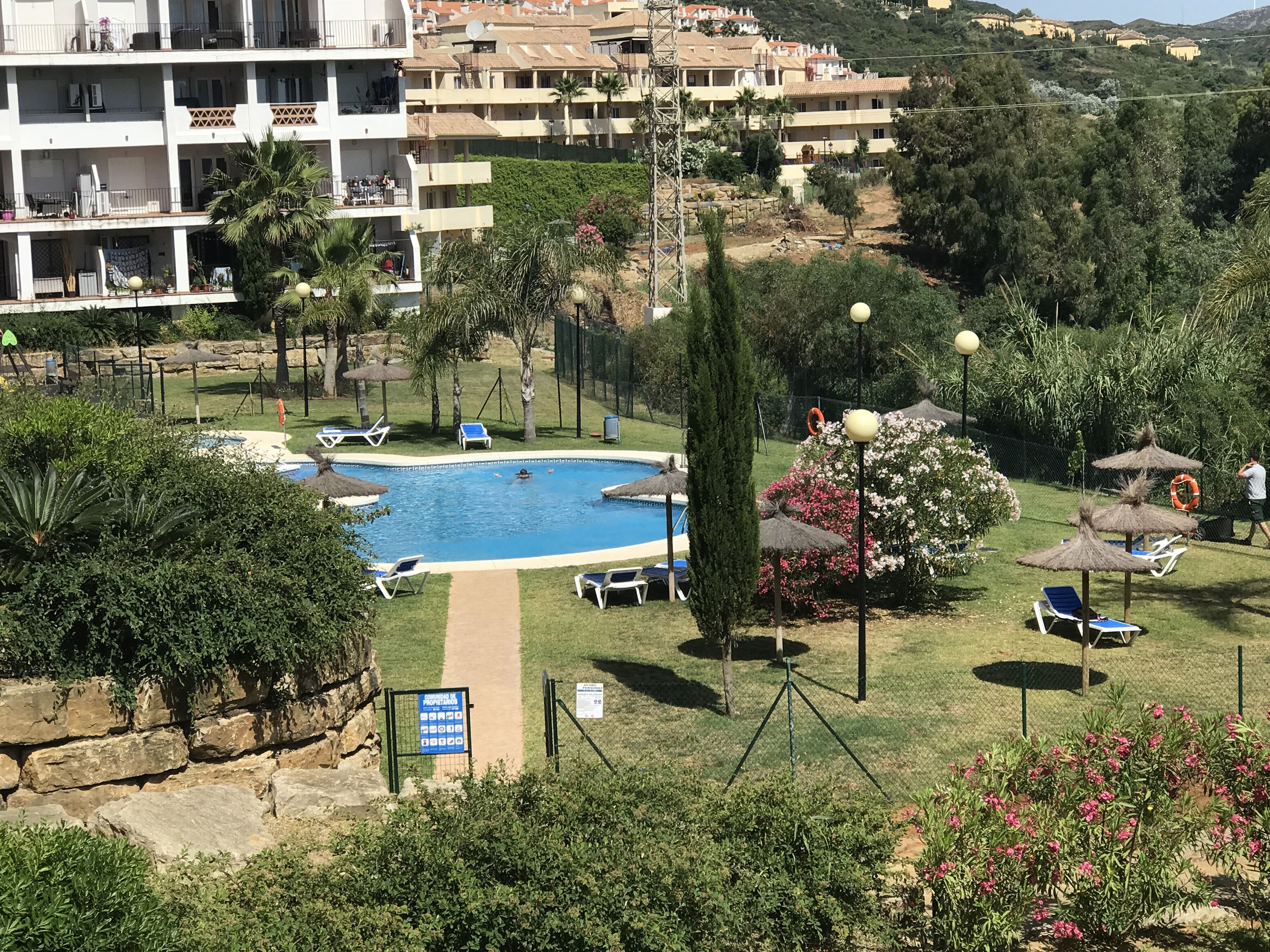A pool area with lounge chairs, a sign indicating amenities, and a view of surrounding buildings.