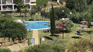A pool area with lounge chairs, a sign indicating amenities, and a view of surrounding buildings. - Manilva Playa luxury apartment with sea view near the beach (Manilva)