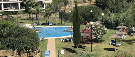 A pool area with lounge chairs, a sign indicating amenities, and a view of surrounding buildings.
