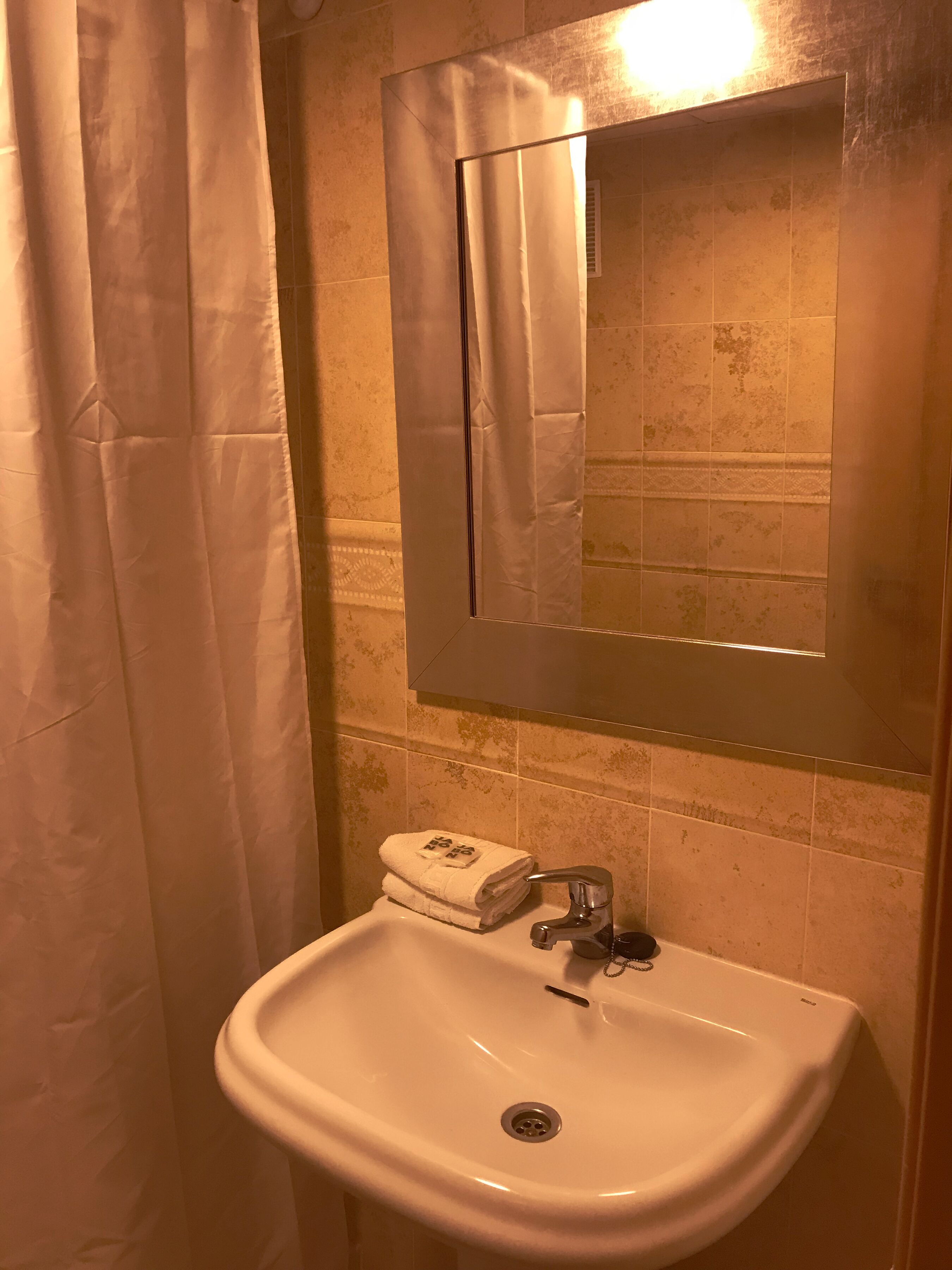 A bathroom with a white sink, a mirror, and a towel dispenser.
