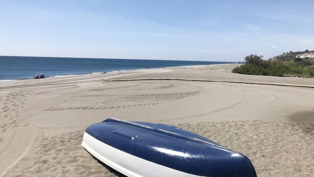 A beach with a boat on the sand, a clear sky, and distant buildings. - Manilva Playa luxury apartment with sea view near the beach (Manilva)