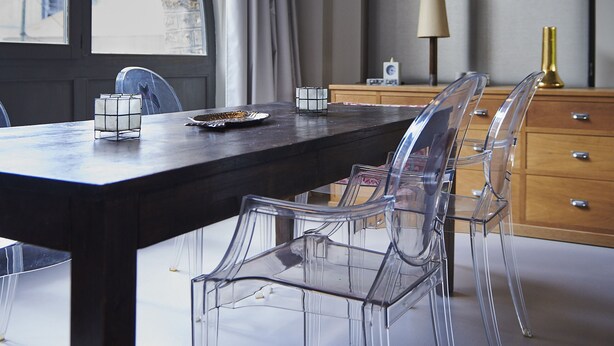 Un comedor moderno con una mesa grande, sillas transparentes, lámparas colgantes y vistas amplias por un ventanal.