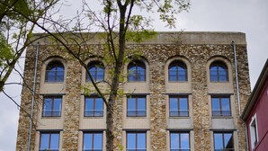 Un edificio de varios pisos con fachada de piedra, amplios ventanales en arco y un pequeño jardín delantero.