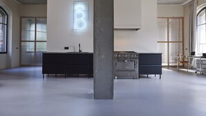 Una cocina moderna con una isla grande, una estufa de acero inoxidable y un letrero de neón con una corona y la letra B.