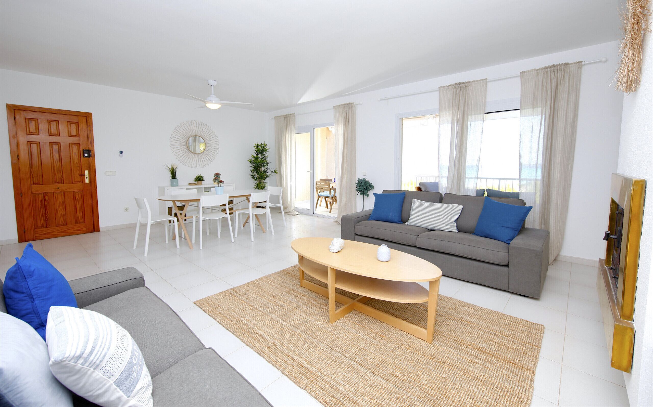 Un salon moderne avec un canapé gris, des chaises blanches, une table basse en bois et un coin repas comprenant une table et des chaises blanches.