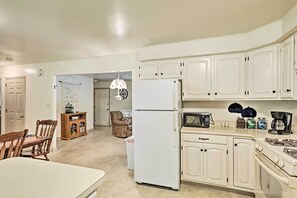 A kitchen with white cabinets, a refrigerator, a stove, and a microwave. There is a dining table with chairs and a wooden cabinet with glass doors.