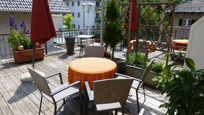 A wooden deck with outdoor furniture, including a round table and chairs, surrounded by potted plants and a red umbrella. - Hotel Alpenrose (Bad Woerishofen)