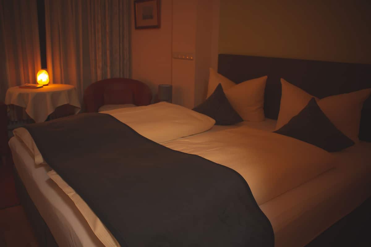 Una habitación de hotel con una cama grande, una mesita de noche, una silla y una lámpara.