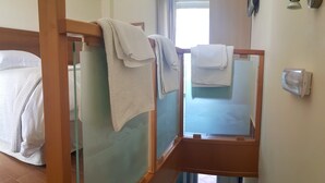 Camera d'albergo con due letti, ciascuno con una testiera in legno e un divisorio in vetro. Sui letti ci sono degli asciugamani e un lampadario fissato al muro.