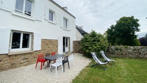 Een wit huis met een grindpad, een tafel met stoelen en twee lounge fauteuils.