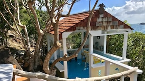 A wooden deck with a pool, surrounded by trees and a view of the ocean. - Two for One! Charming Cottage on hillside with private lounge on Turtle Beach! (BASSETERRE)