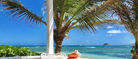 A wooden table with a seashell, white wicker chairs, and a view of the ocean with a distant island.