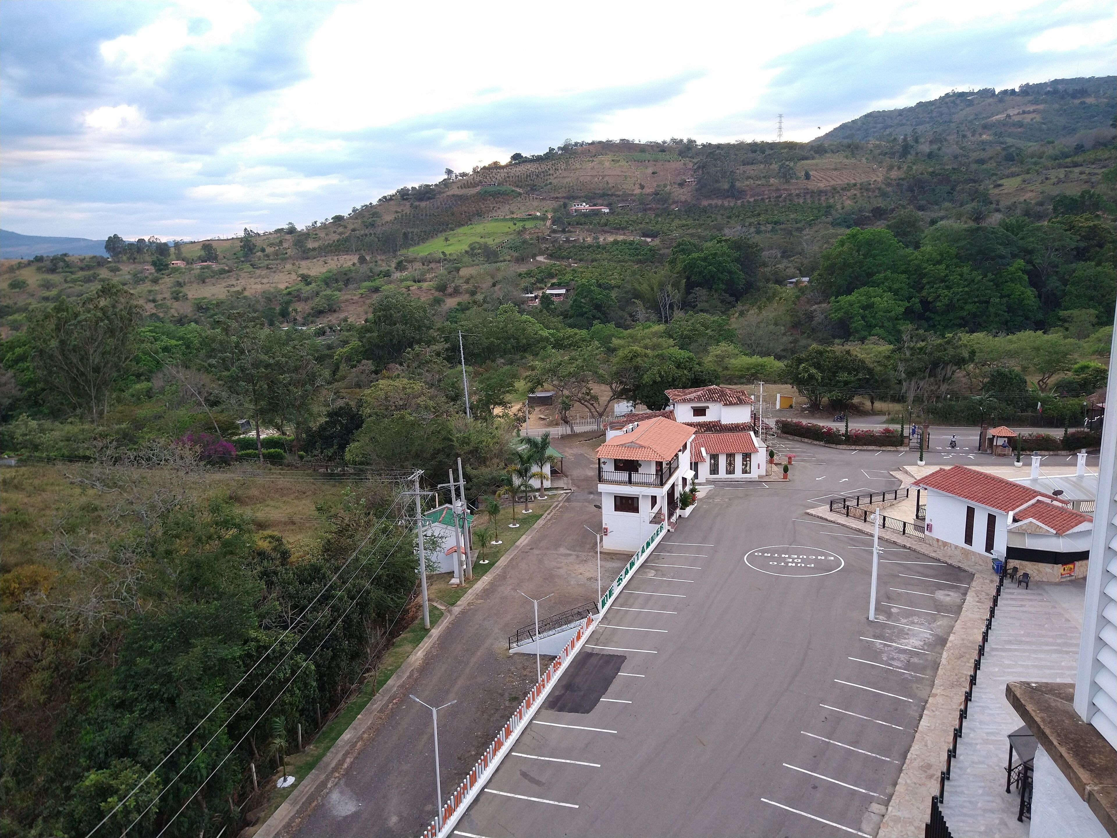 Un estacionamiento con espacios delimitados, un edificio con techo de tejas rojas y un paisaje montañoso al fondo.
