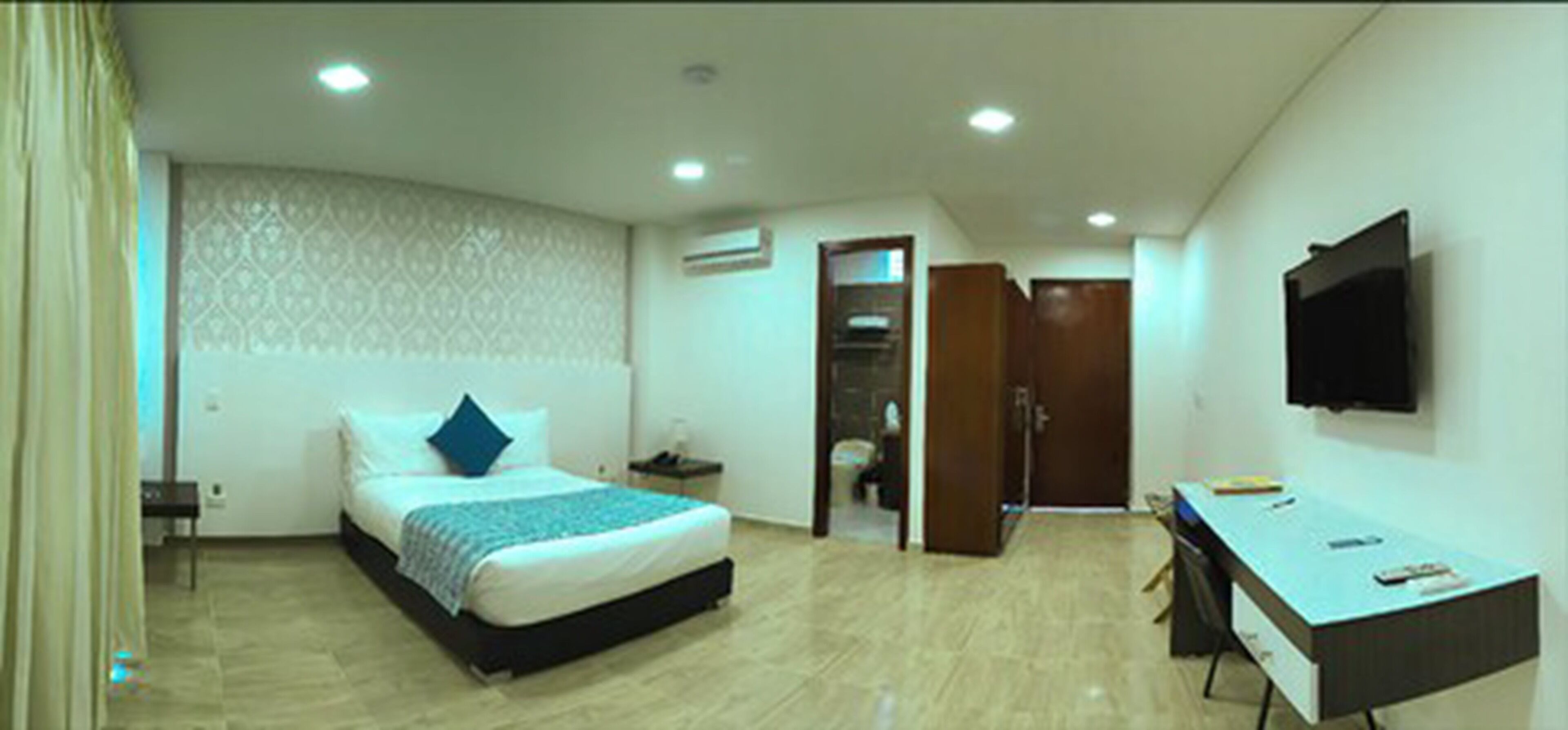 Een hotelkamer met een bed, bureau, televisie en airconditioning.