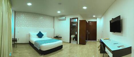 Een hotelkamer met een bed, bureau, televisie en airconditioning.