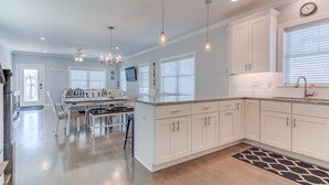 Una cocina moderna con armarios blancos, una zona de comedor con mesa y sillas, e iluminación colgante.