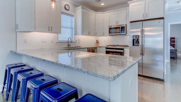 Una cocina moderna con armarios blancos, un refrigerador de acero inoxidable, un microondas y una isla grande con taburetes de bar azules.