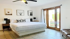 Une chambre dotée d’un grand lit, de deux tables de chevet avec des lampes, d’un ventilateur de plafond et d’une porte-fenêtre coulissante donnant sur un espace extérieur.