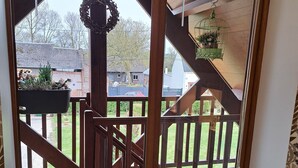 Una escalera de madera conduce a una terraza con barandilla, un farol colgante y vistas a un patio trasero con una casa y un coche.