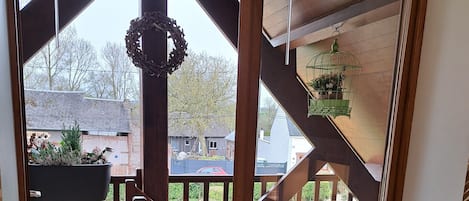 Una escalera de madera conduce a una terraza con barandilla, un farol colgante y vistas a un patio trasero con una casa y un coche.