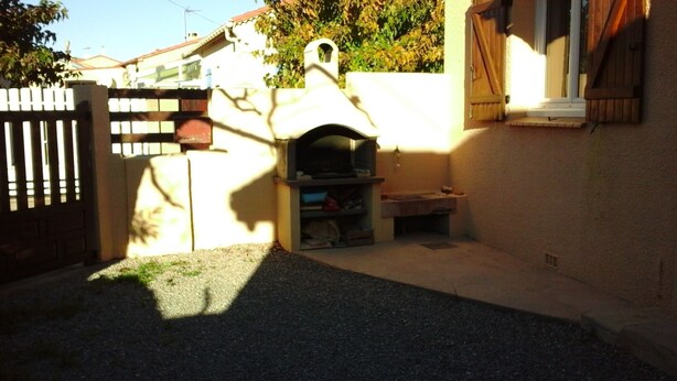Ein Garten mit einem Steinofen, einem Holzzaun und einem Haus mit einem Fenster.