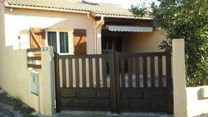 Ein Haus mit geschlossenem Eingangstor, einem Ziegeldach und einer kleinen Veranda mit weißem Sonnendach.
