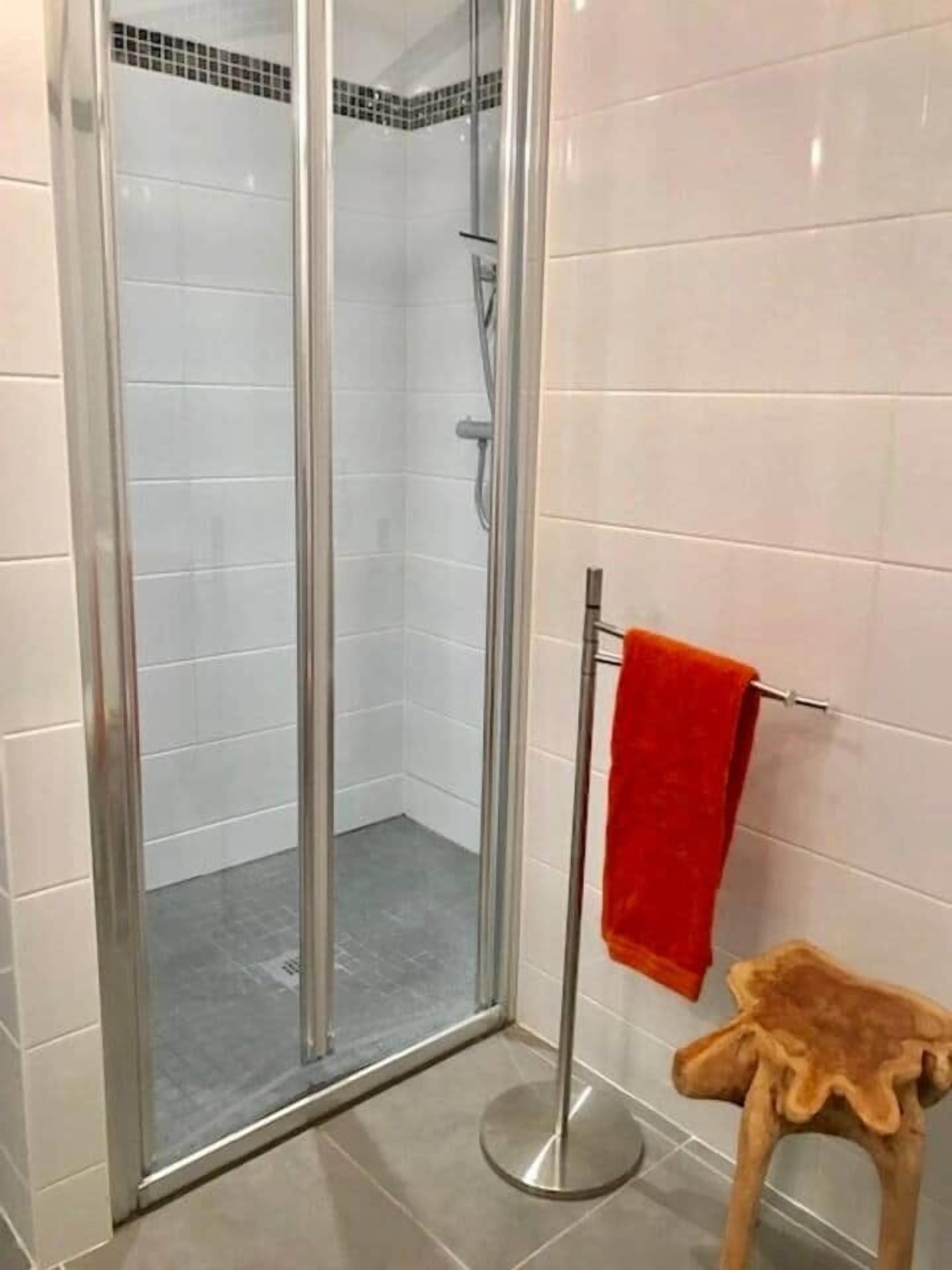 A shower area with a glass door, a red towel on a rack, and a small stool.