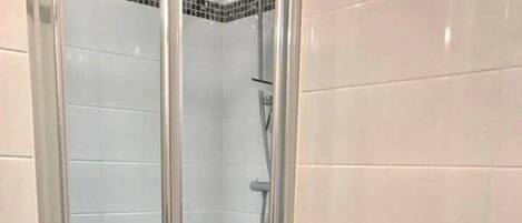 A shower area with a glass door, a red towel on a rack, and a small stool.