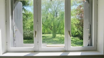 A window with three white-framed glass panes, each with a vertical metal handle, overlooking a green landscape with trees and a lawn.