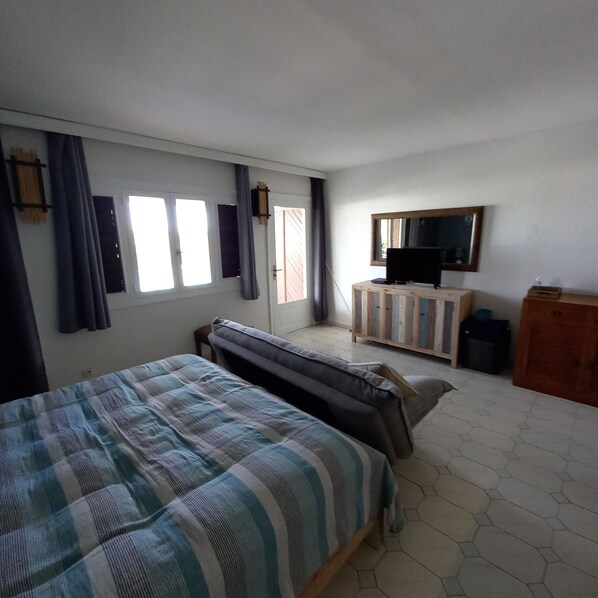 A bedroom with a bed, a TV on a wooden cabinet, and a window with curtains. - Charming apartment, quiet at the luxury residence "La plantation Saint-Marthe" (saint-francois)