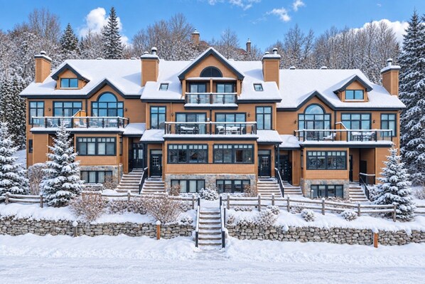 A large, multi-story building with a stone foundation, multiple balconies, and a snow-covered landscape.