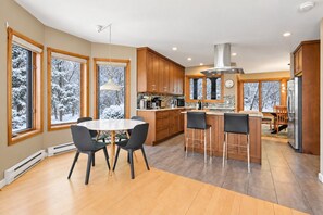A modern kitchen with wooden cabinets, a central island, and a dining area with a table and chairs. - Tremblant Prestige - Clairiere 406 (Mont-Tremblant)