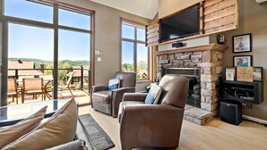 A spacious living room with a stone fireplace, leather sofas, and large windows offering a view of the outdoors.