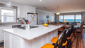Una cucina moderna con mobili bianchi, una grande isola e un'area pranzo con sedie in legno e vista sull'oceano.