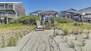 Una proprietà fronte spiaggia con un vialetto sabbioso che conduce a un pontile di legno, immersa nella vegetazione costiera.