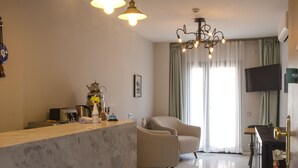 A modern living room with a marble floor, a sofa, a coffee table, and a TV mounted on the wall. - Pharos Hotel (Datça)