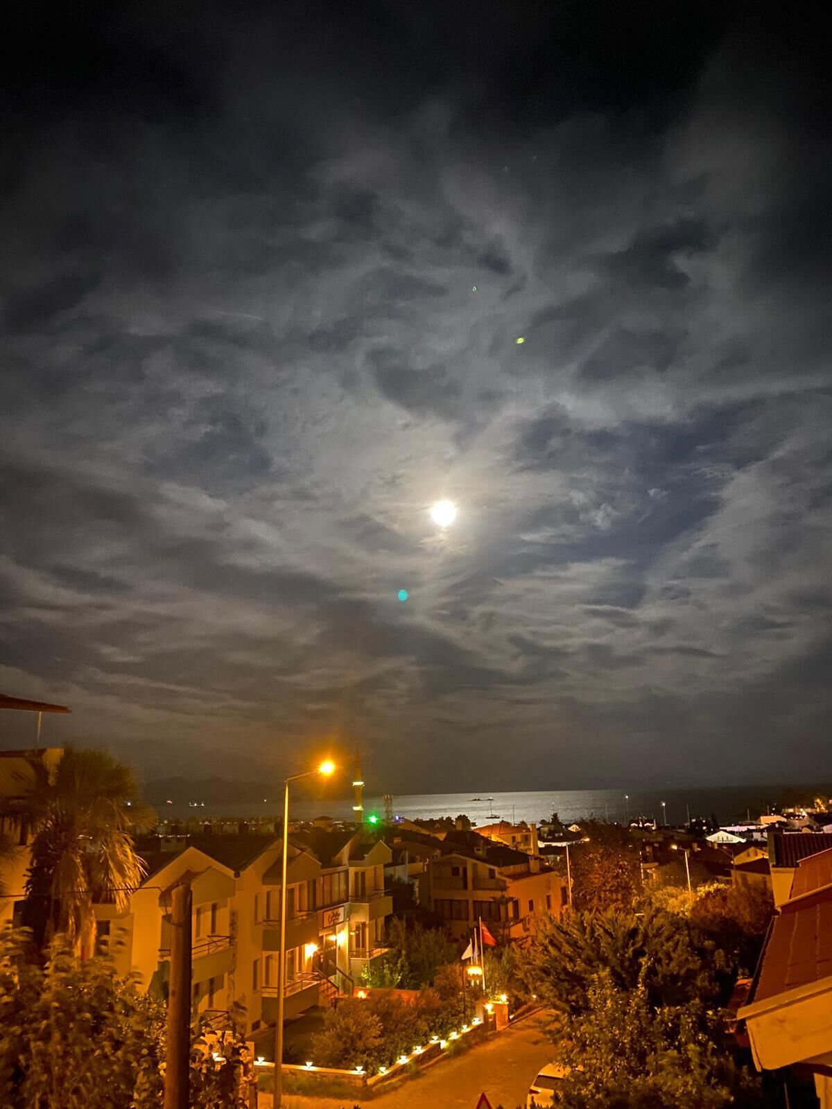 Un pueblo costero de noche con luna y nubes visibles.