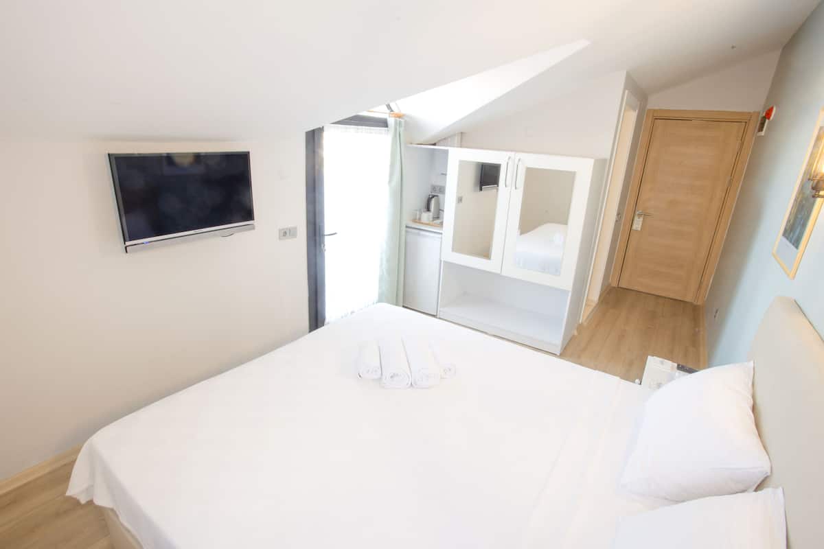 Un dormitorio con una cama, un televisor instalado en la pared y una zona de kitchenette.