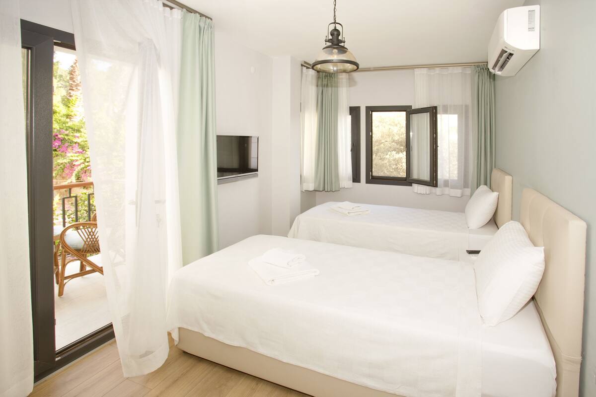 Habitación de hotel con dos camas, televisión y balcón con una silla.