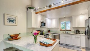 A kitchen with white cabinets, a marble countertop, a wooden stool, and a vase with flowers. - Oyster Haven: Private Oyster Beach w/Kayaks (Shelton)