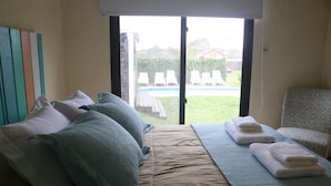 A bedroom with a bed, pillows, a chair, and a view of a swimming pool. - Widow's Inn - Superior Double (Punta del Diablo, Rocha)